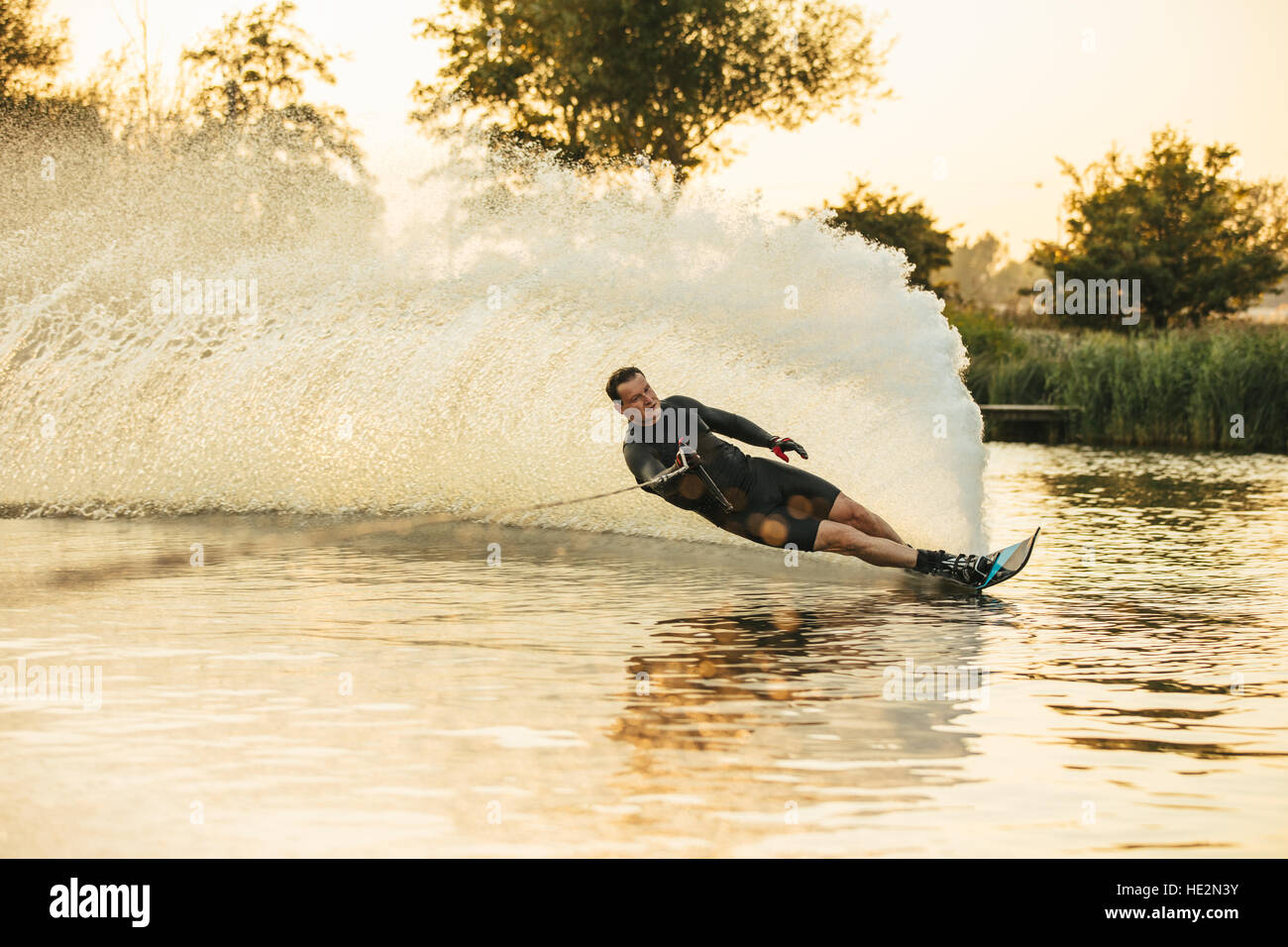 Man show of his water skiing skill on a lake. Athlete doing stunts on wakeboard. Stock Photo