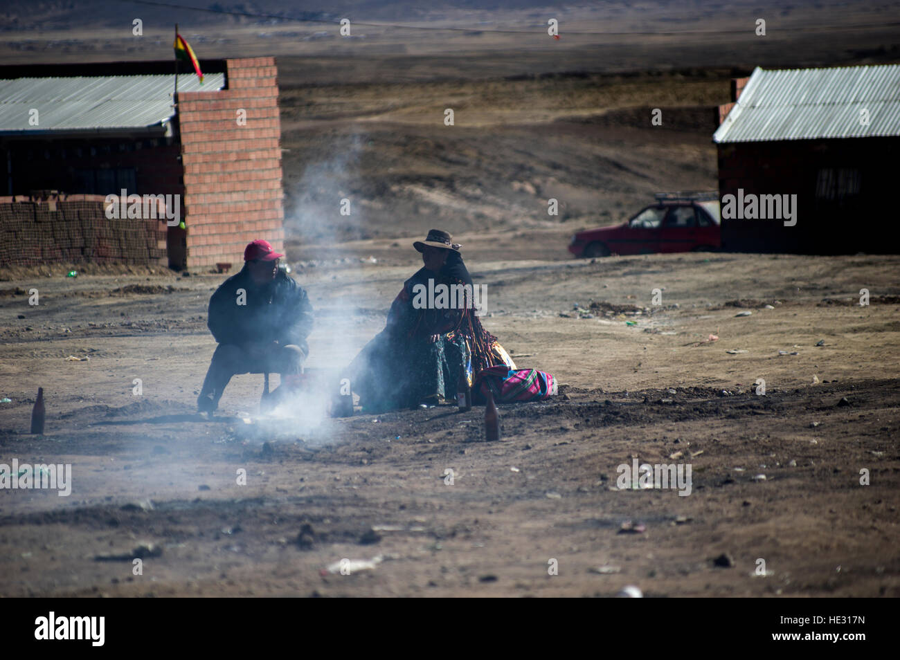 A couple Bolivians, faces obscured by smoke and shadow, sit next to a burning mesa, an August offering to the pachamama Stock Photo
