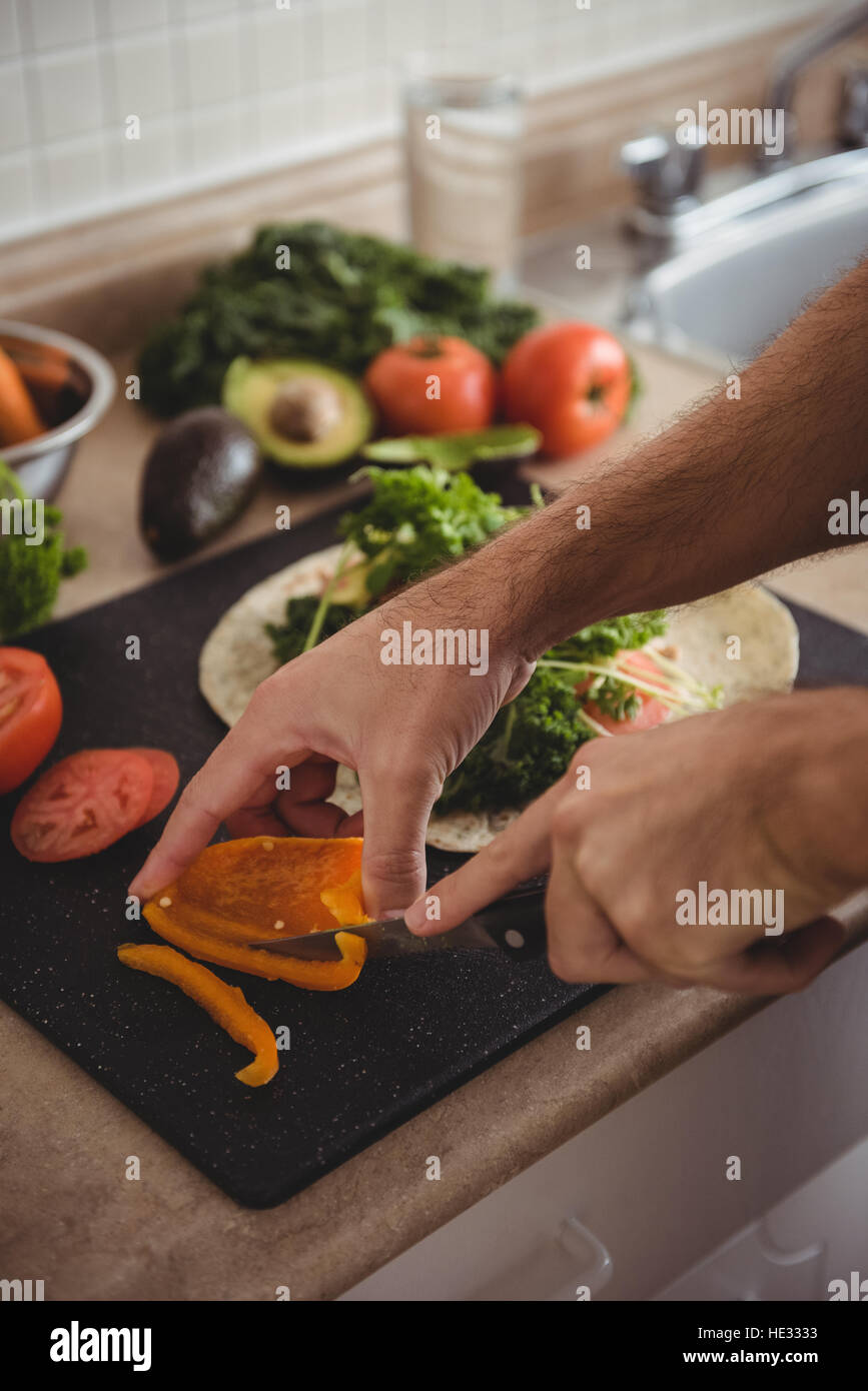 Close-up of mans hand slicing bell pepper on chopping board in the ...