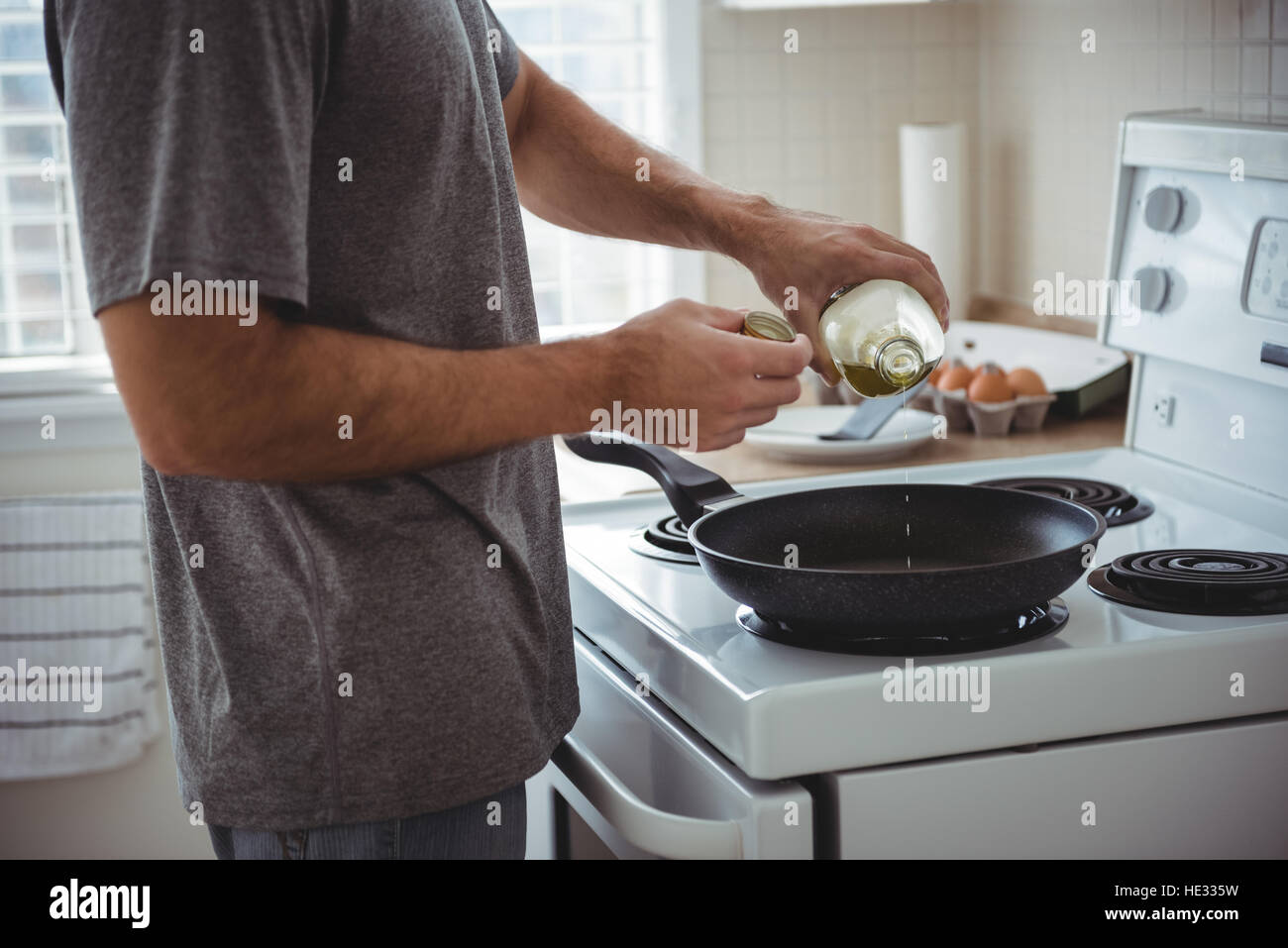 Mid section of man pouring olive oil into the frying pan in the kitchen