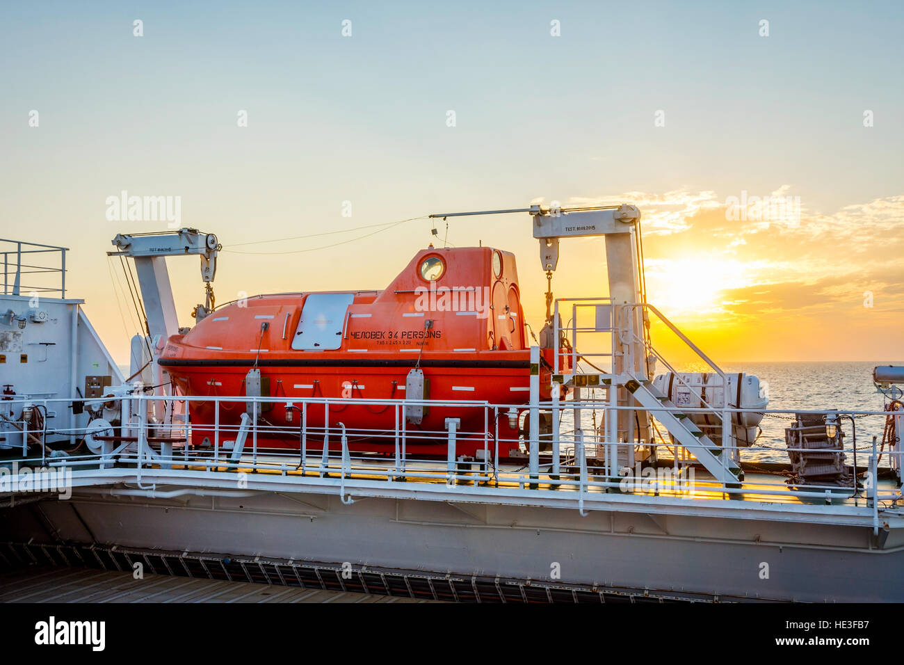 Orange rescue boat on the cargo vessel at the sea in sunset Stock Photo