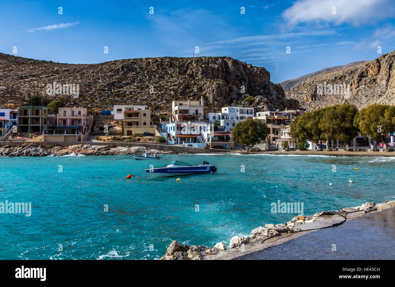 Small blue speedboat on aquamarine sea with Greek style houses surrounding bay Stock Photo