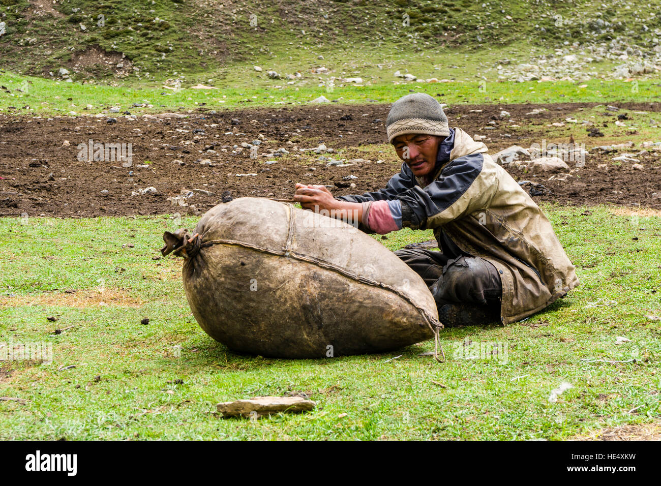 A yak herder is making butter from yak milk on the meadows around Ice Lake Stock Photo