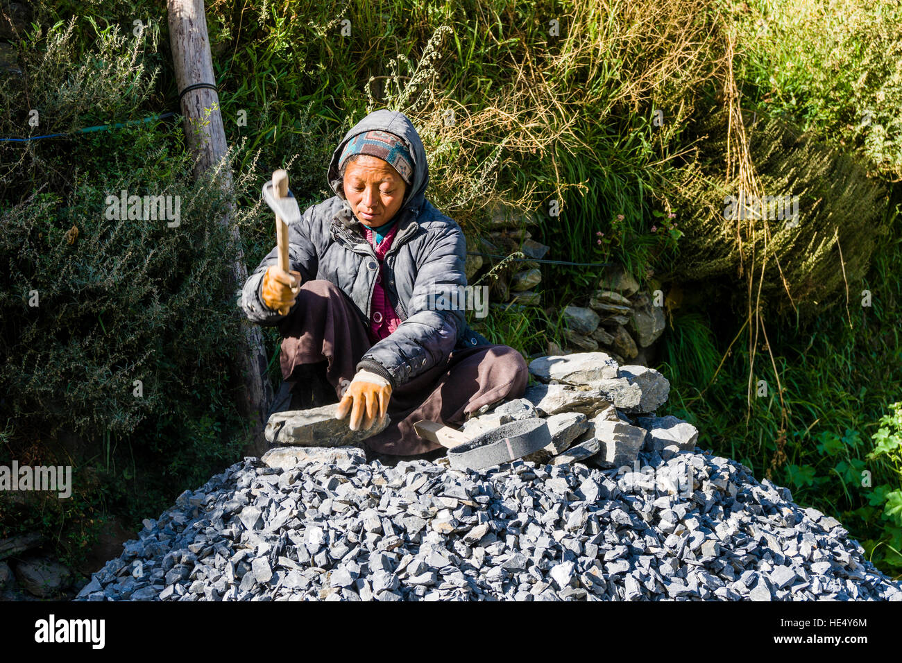 A local woman is cutting rocks by hand, using a hammer Stock Photo