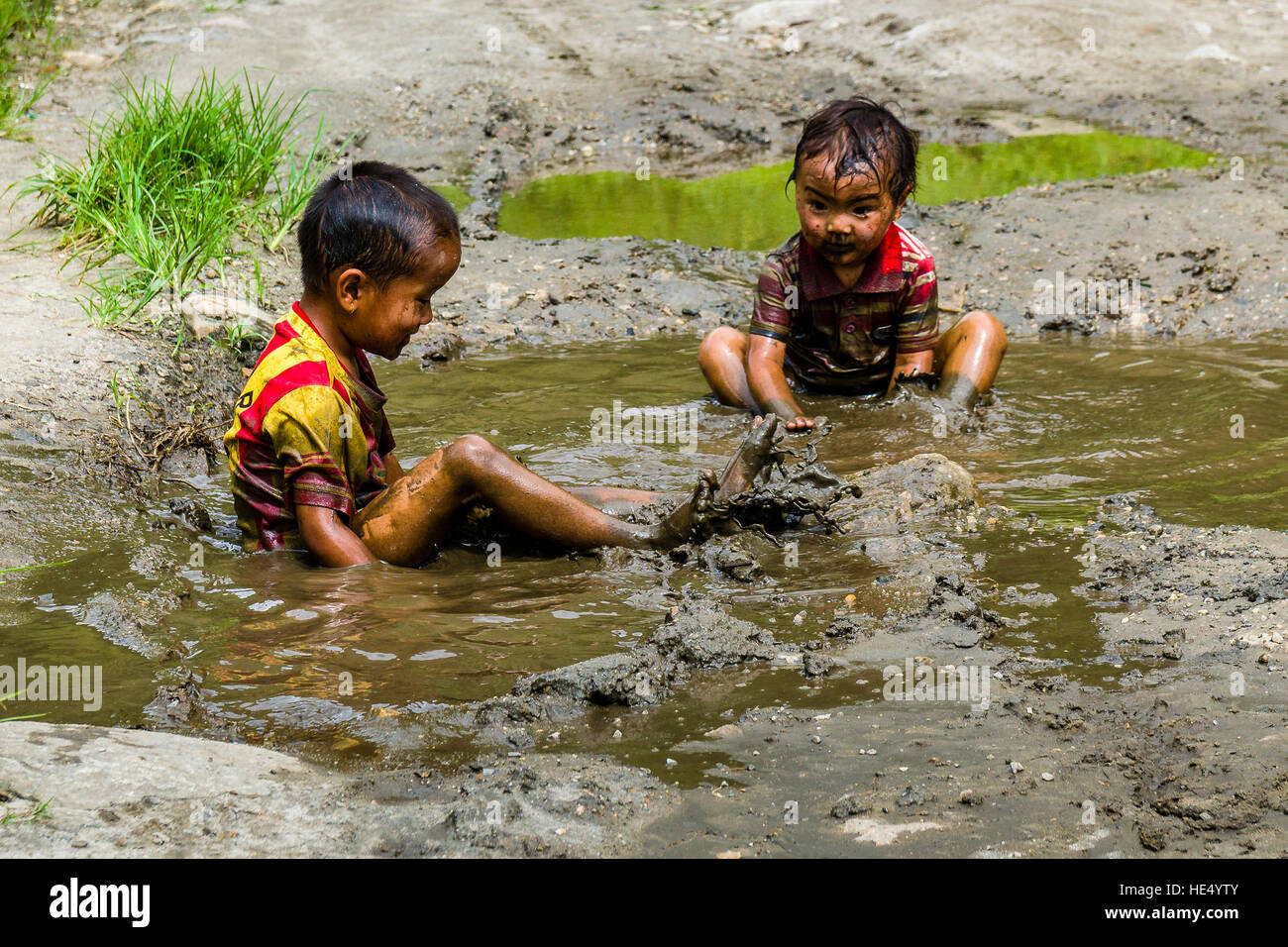 Two local boys, only wearing shirts, are playing in the mud of a waterhole Stock Photo