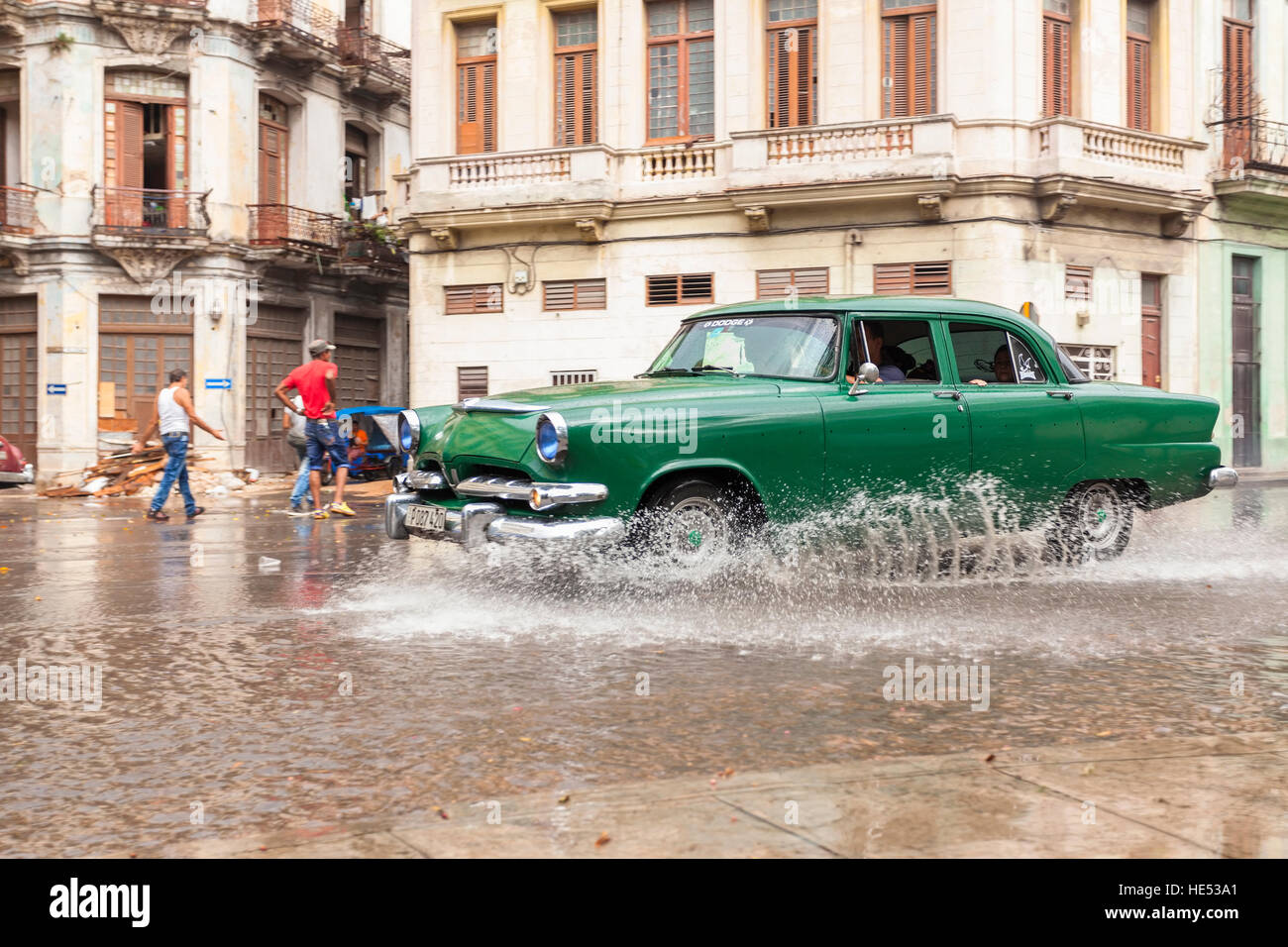 A green classic car passes through a puddle after a a heavy rainfall in Old Havana, Cuba. Stock Photo