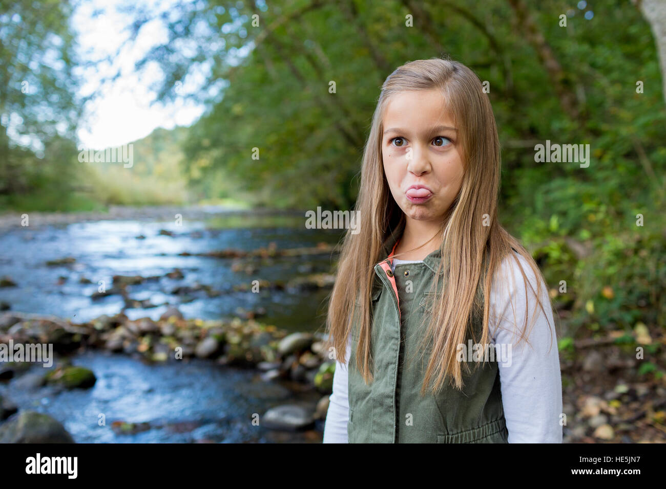 Young girl in a green vest posing for a lifestyle portrait outdoors along the banks of the McKenzie River in Oregon. Stock Photo