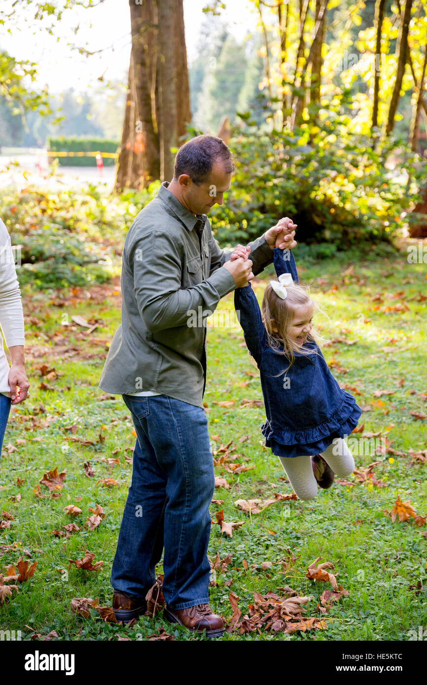 Dad swinging his young daughter around by the arms while playing and having fun at a nature park. Stock Photo
