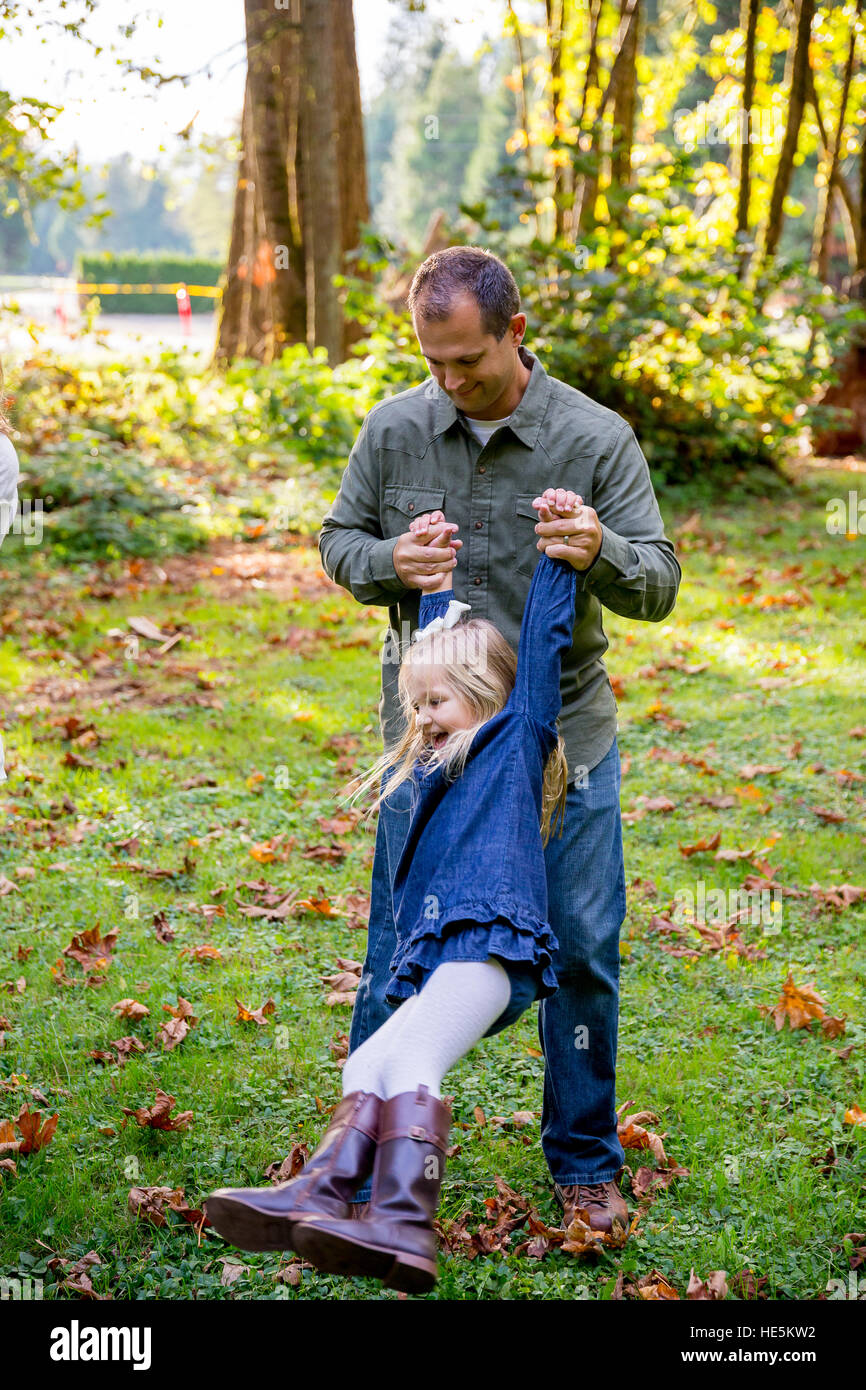 Dad swinging his young daughter around by the arms while playing and having fun at a nature park. Stock Photo