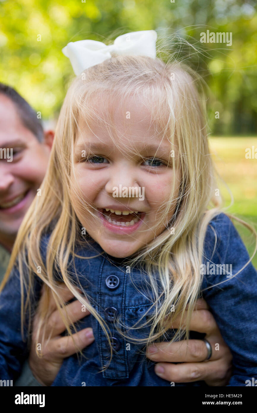 Young girl laughing and smiling while her dad holds her up for the camera. Stock Photo