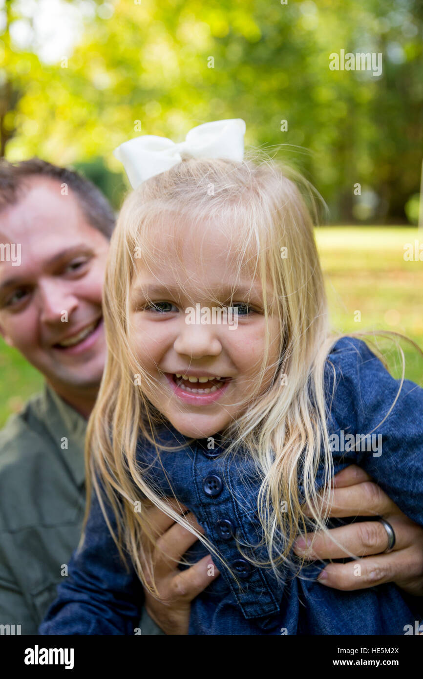 Young girl laughing and smiling while her dad holds her up for the camera. Stock Photo