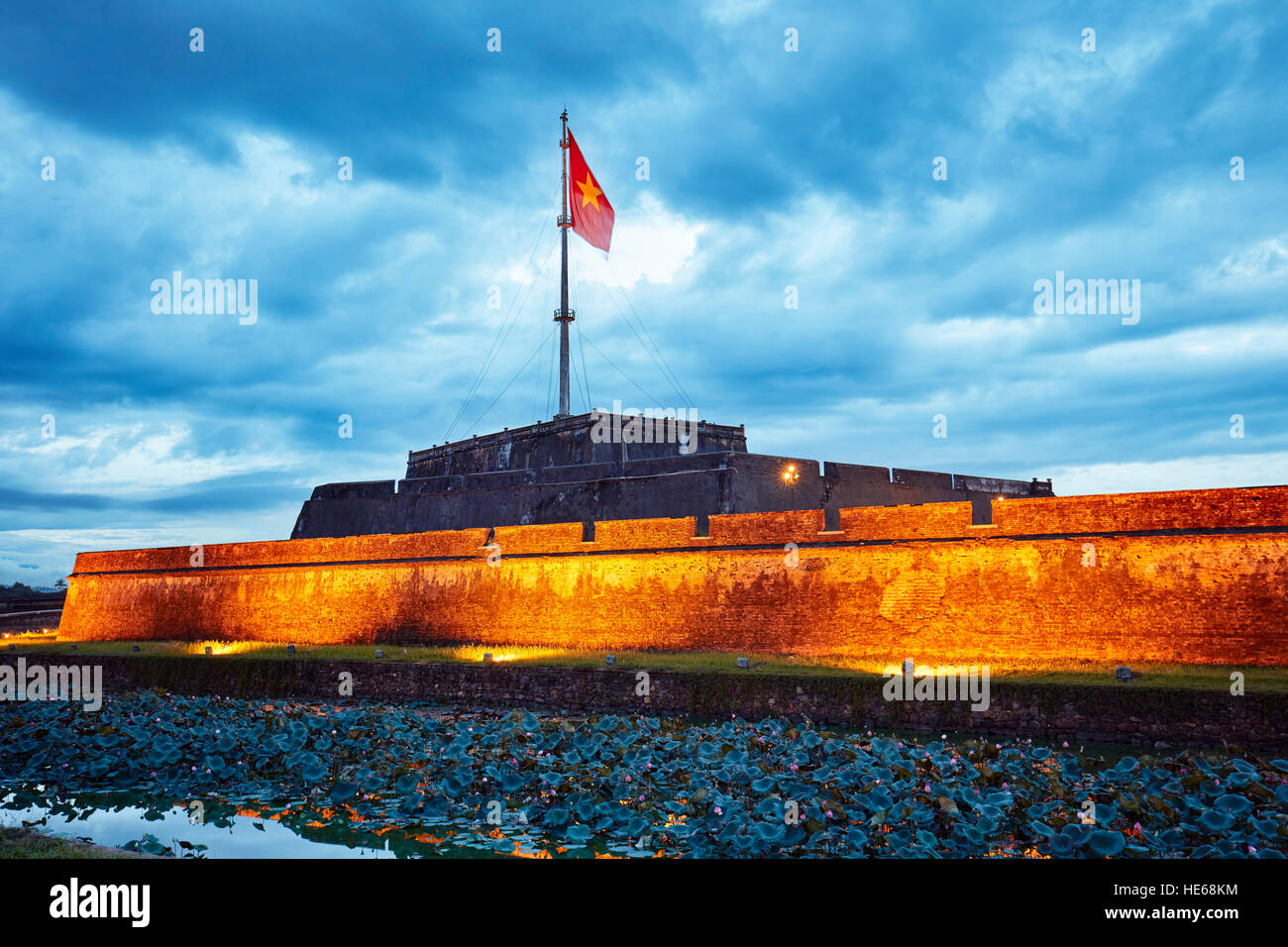 National flag of Vietnam flowing on top of the Flag Tower in the Imperial City at dusk. Hue, Vietnam. Stock Photo