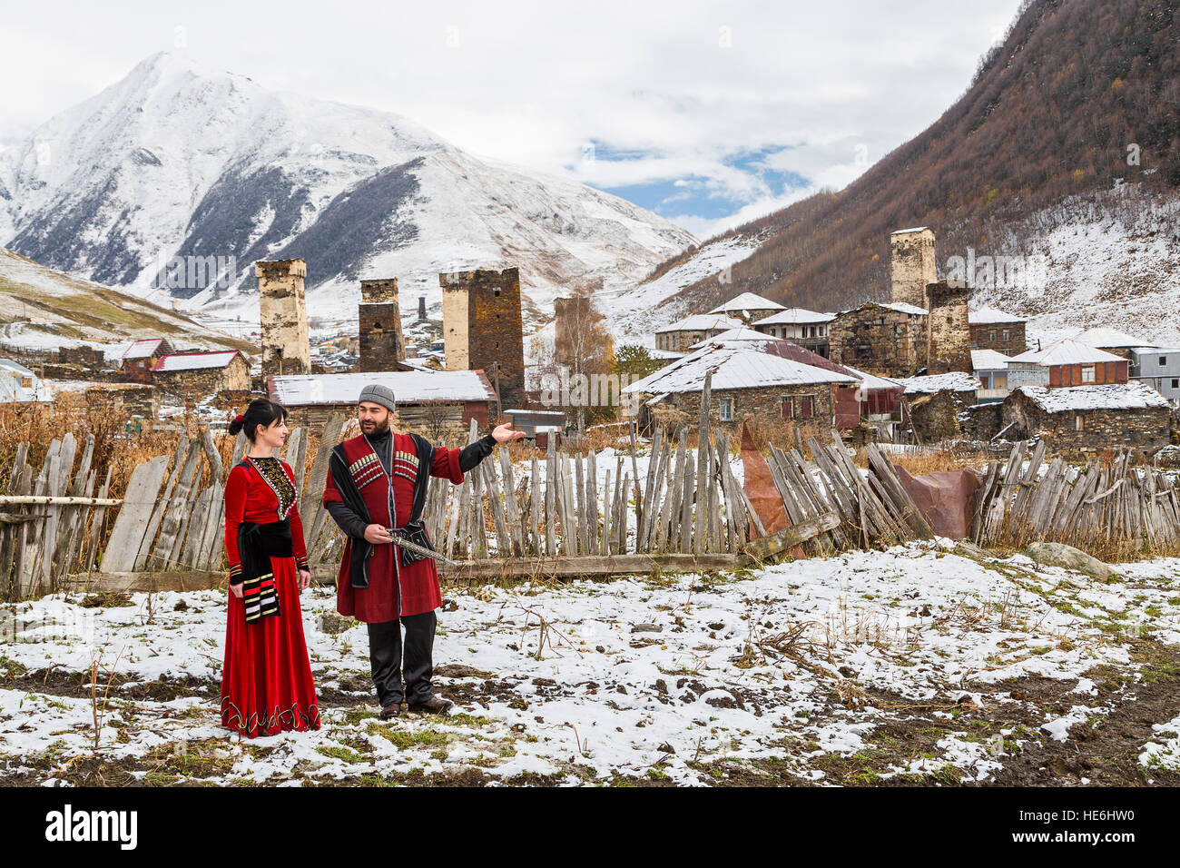 Georgian couple in national costumes in Ushguli, Georgia. Caucasus mountains and medieval towers are seen on the background. Stock Photo