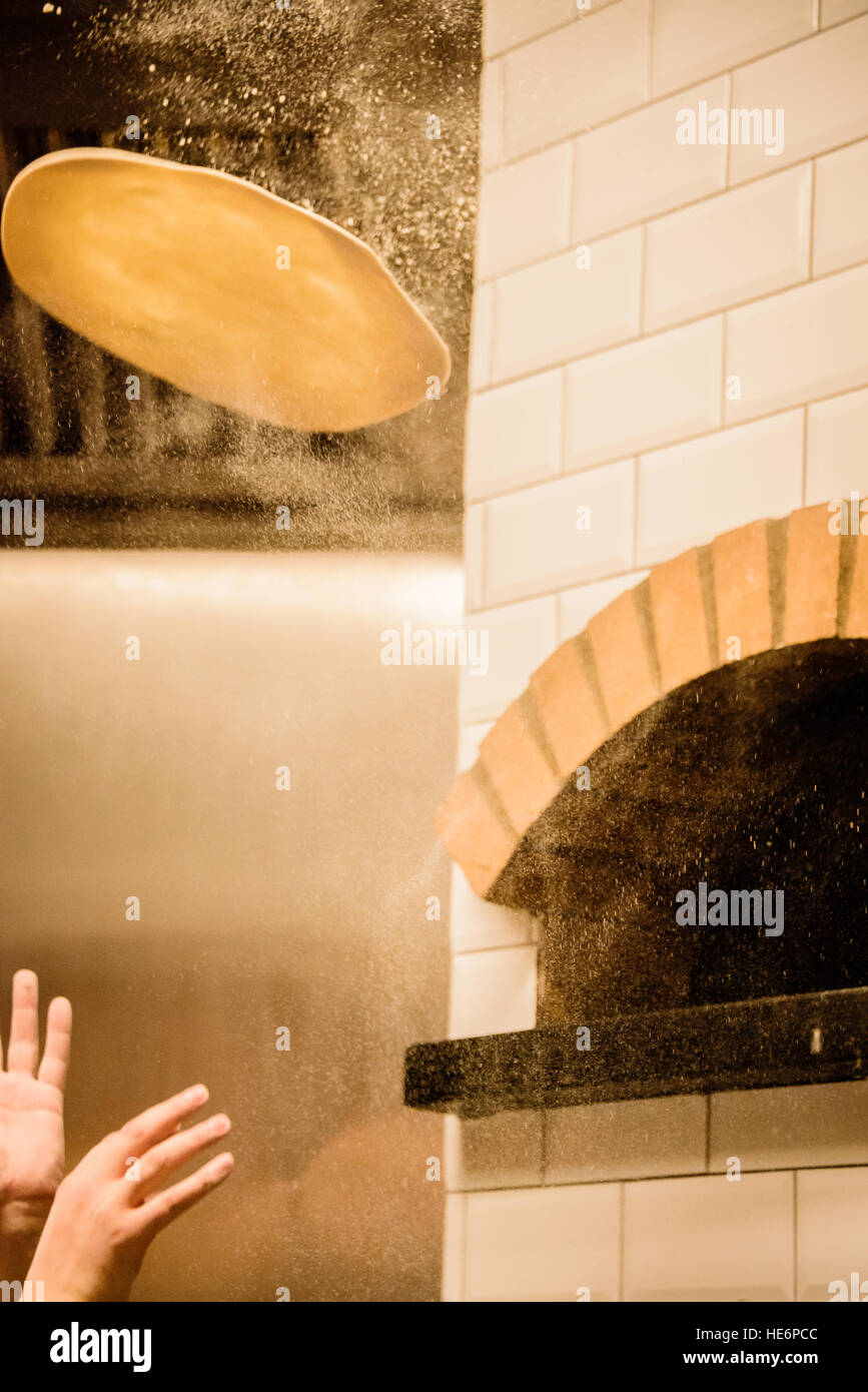 Pizza base being thrown in front of Pizza oven Stock Photo