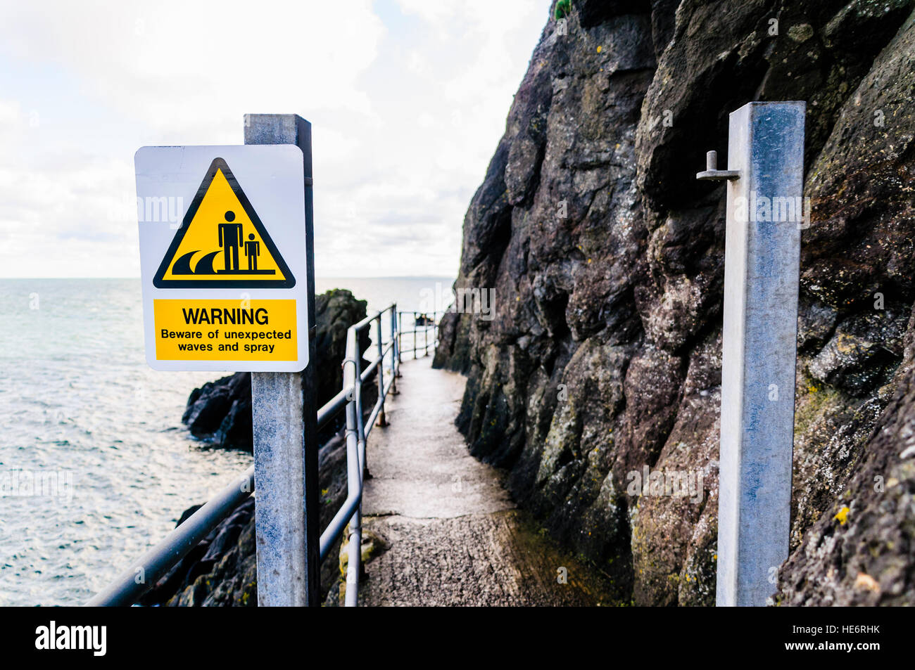 Sign at a coastal path warning people about the possibility of unexpected waves. Stock Photo