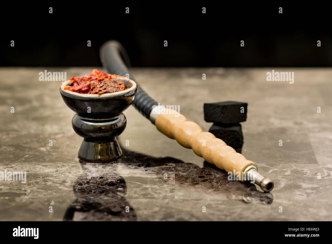 Hookah head with tobacco inside and pipe and coals on the table with