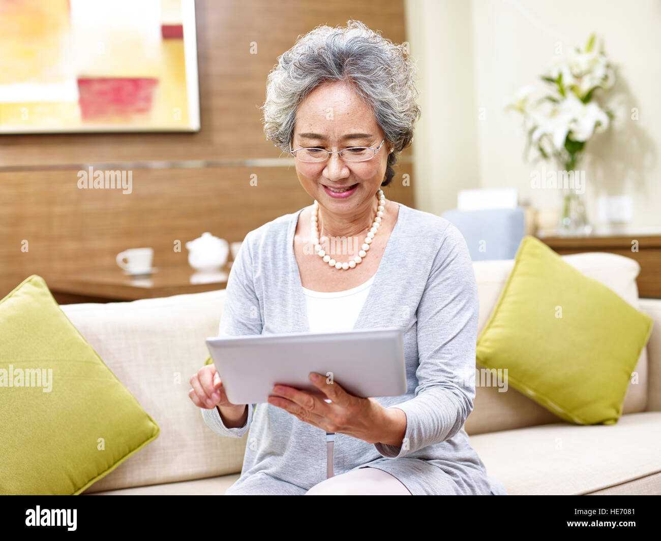 senior asian woman sitting on couch at home using a tablet computer. Stock Photo