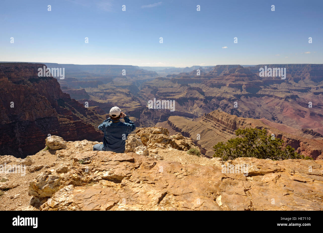 Adventure travel man at edge of the Grand Canyon south rim Pipe Creek Vista taking photo, Arizona USA rear view looking out over majestic Grand Canyon Stock Photo