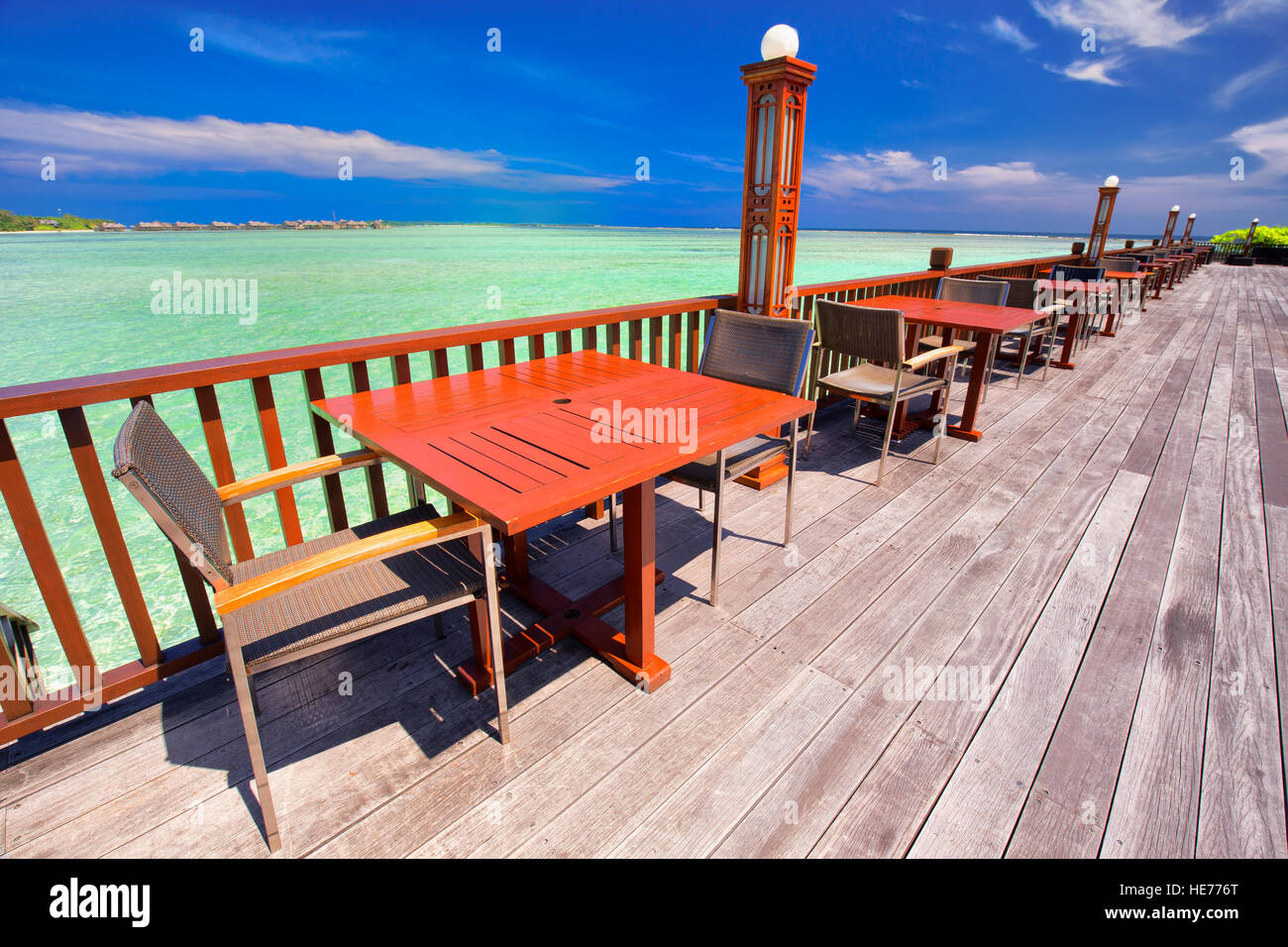 Chairs and tables with palm trees, water bungalows and clear water on luxurious beach resort. Stock Photo