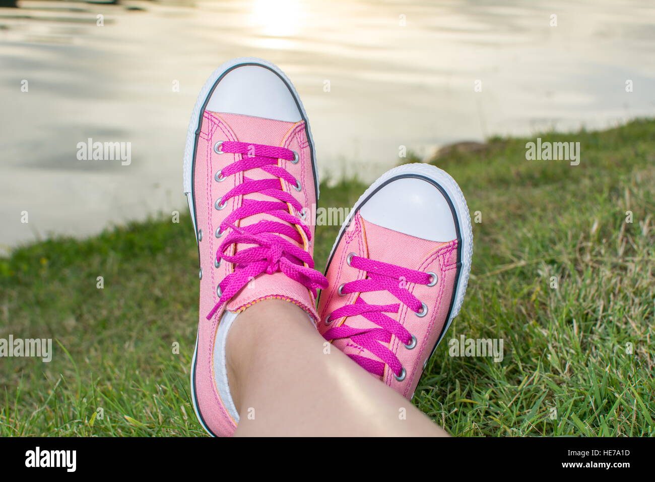 Enjoying by the lake. Woman legs wearing pink sneakers Stock Photo