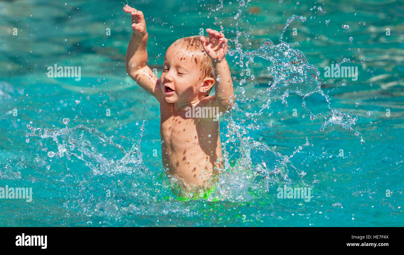 Funny photo of active baby boy splashing in swimming pool with fun