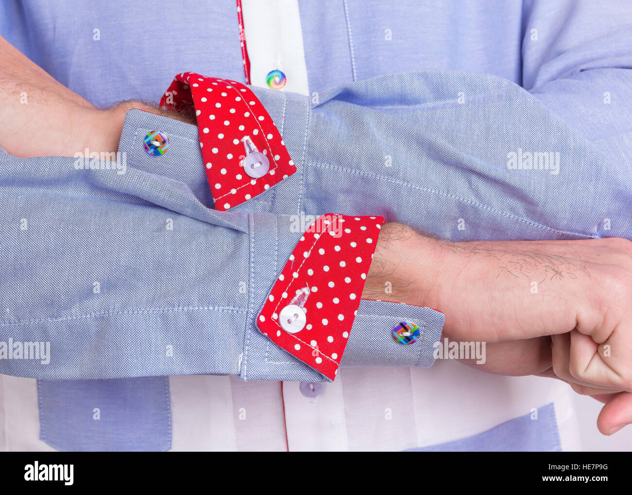 Stylish man dressed in a blue formal shirt, detail close-up of sleeves inc red polkadot cuffs and rainbow buttons Stock Photo