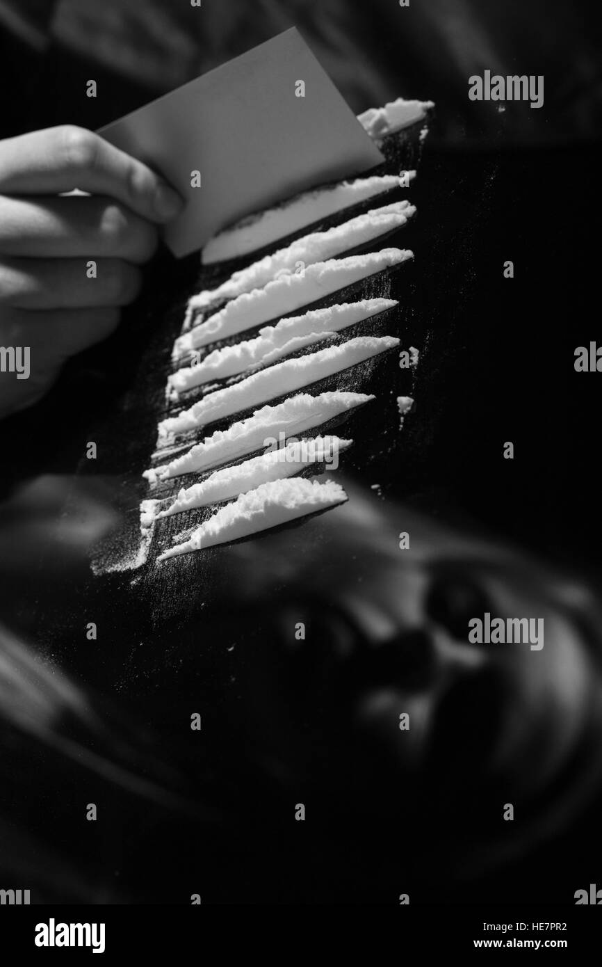 cocaine or other drugs cut with card on mirror with female reflection, hand dividing white powder narcotic, monochrome Stock Photo