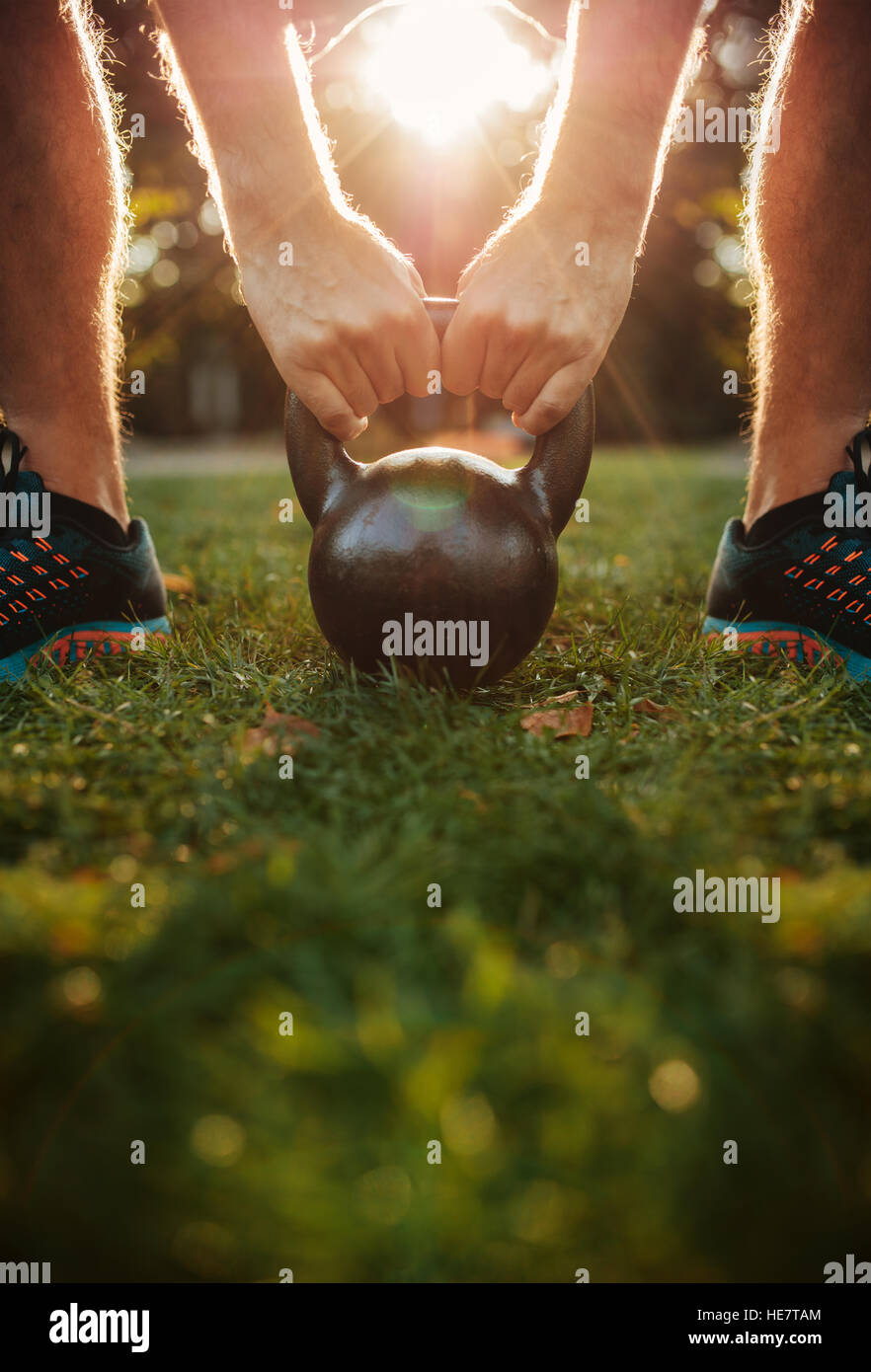 Cropped shot of young man doing kettlebell workout, focus on hands holding kettle bell on grass. Stock Photo