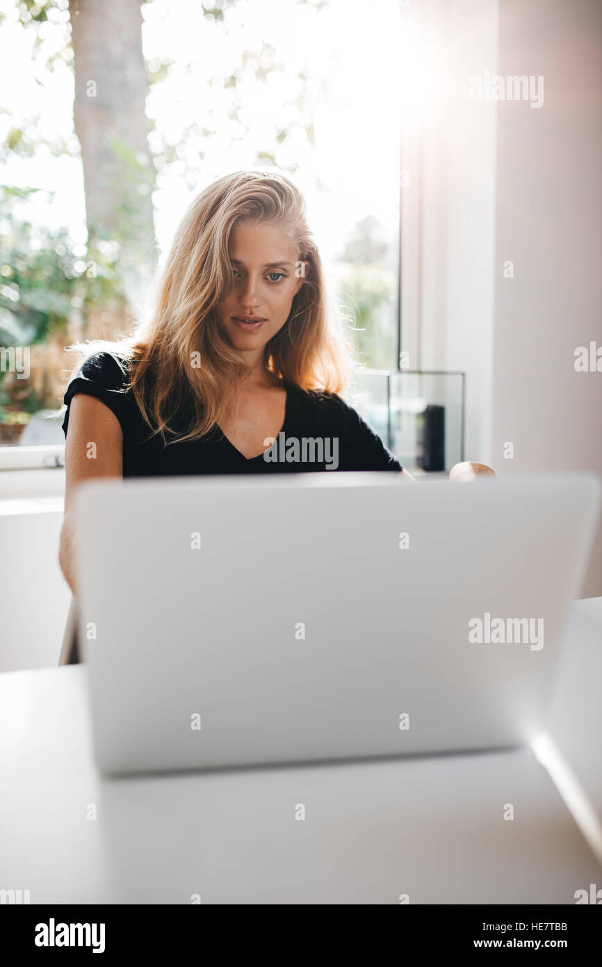 Young woman working on laptop at home in the morning. Beautiful female surfing the net on laptop computer. Stock Photo