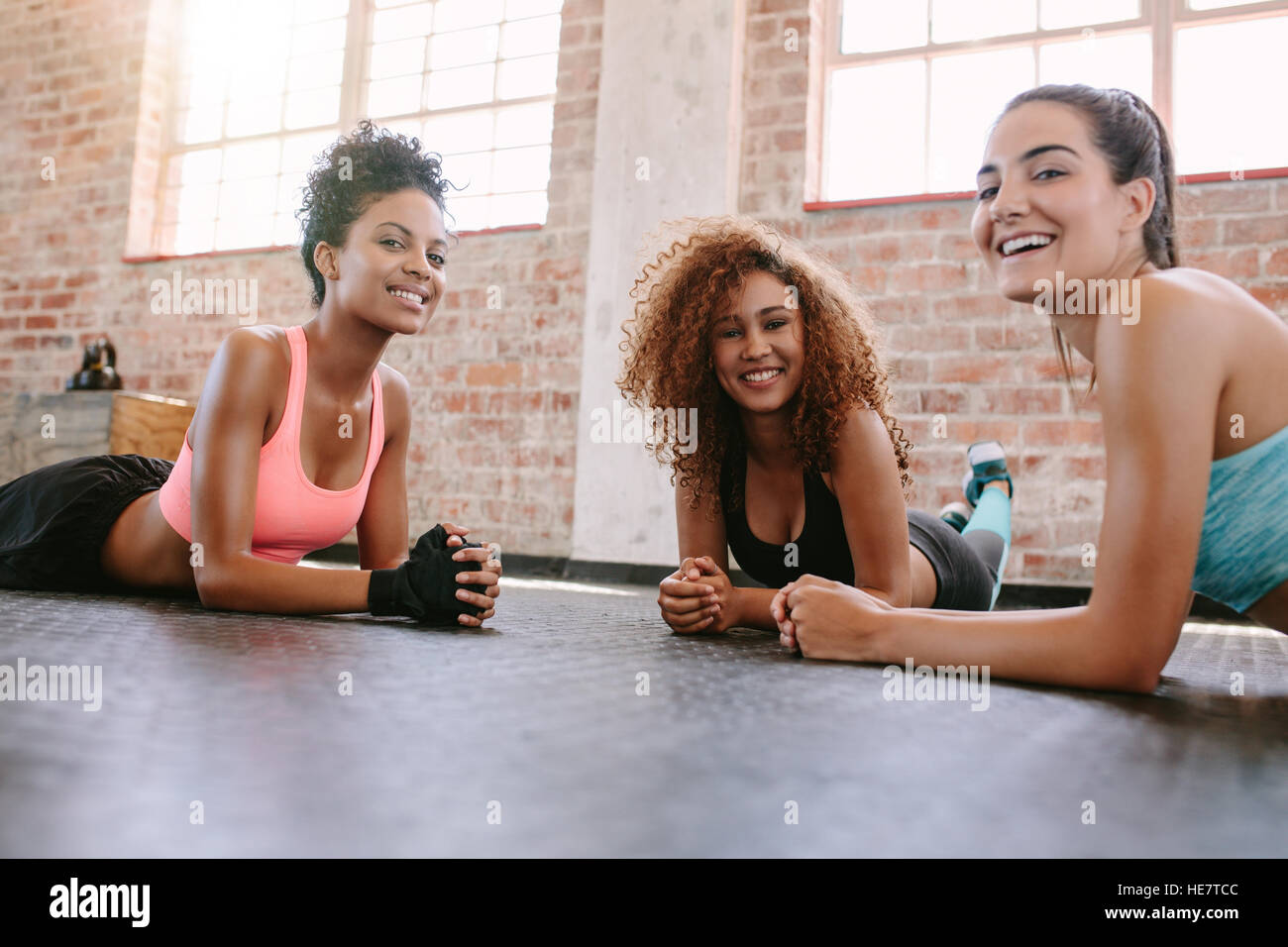 Portrait of three young women in fitness class looking at camera and smiling. Female friends exercising together in fitness class. Stock Photo