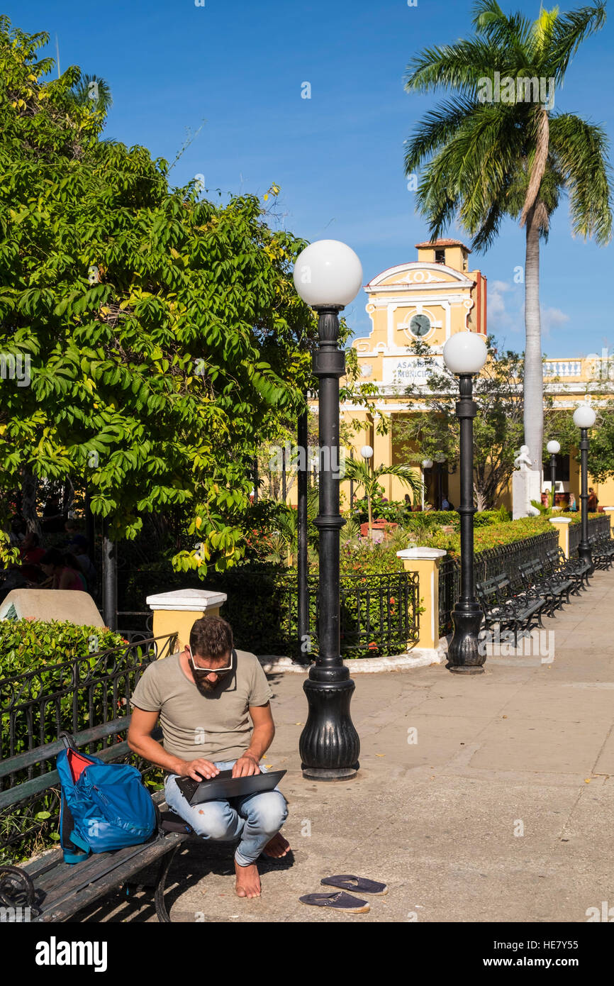 Man using laptop computer on park bench, Parque Cespedes, wifi zone, hotspot, Trinidad, Cuba Stock Photo