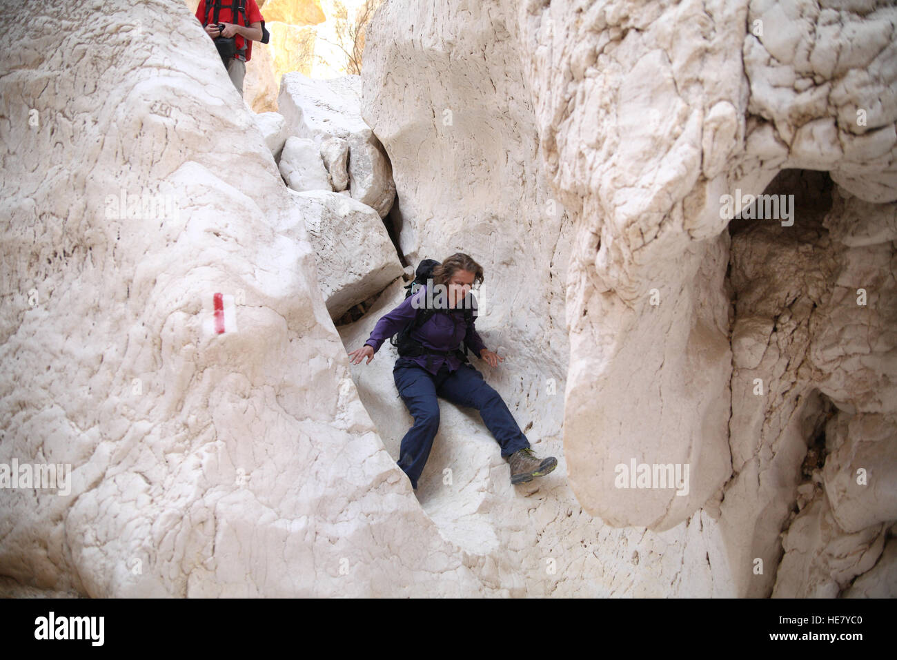 A senior citizen 53 year old woman hiker slides down a dangerous and