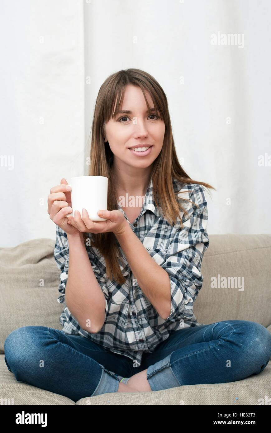 Portrait of young woman sitting on couch in her living room and ...