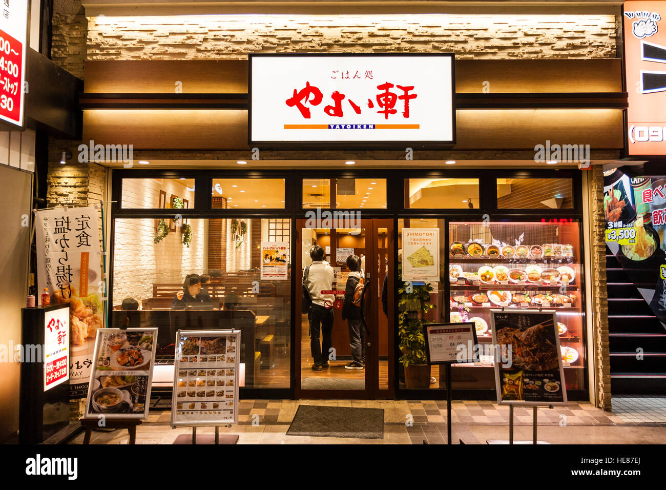 Japan, Kumamoto, Shimotori Arcade Street. Yayoi, known as Yayoiken, Japanese Teishoku restaurant chain. Entrance, night time, people inside. Stock Photo