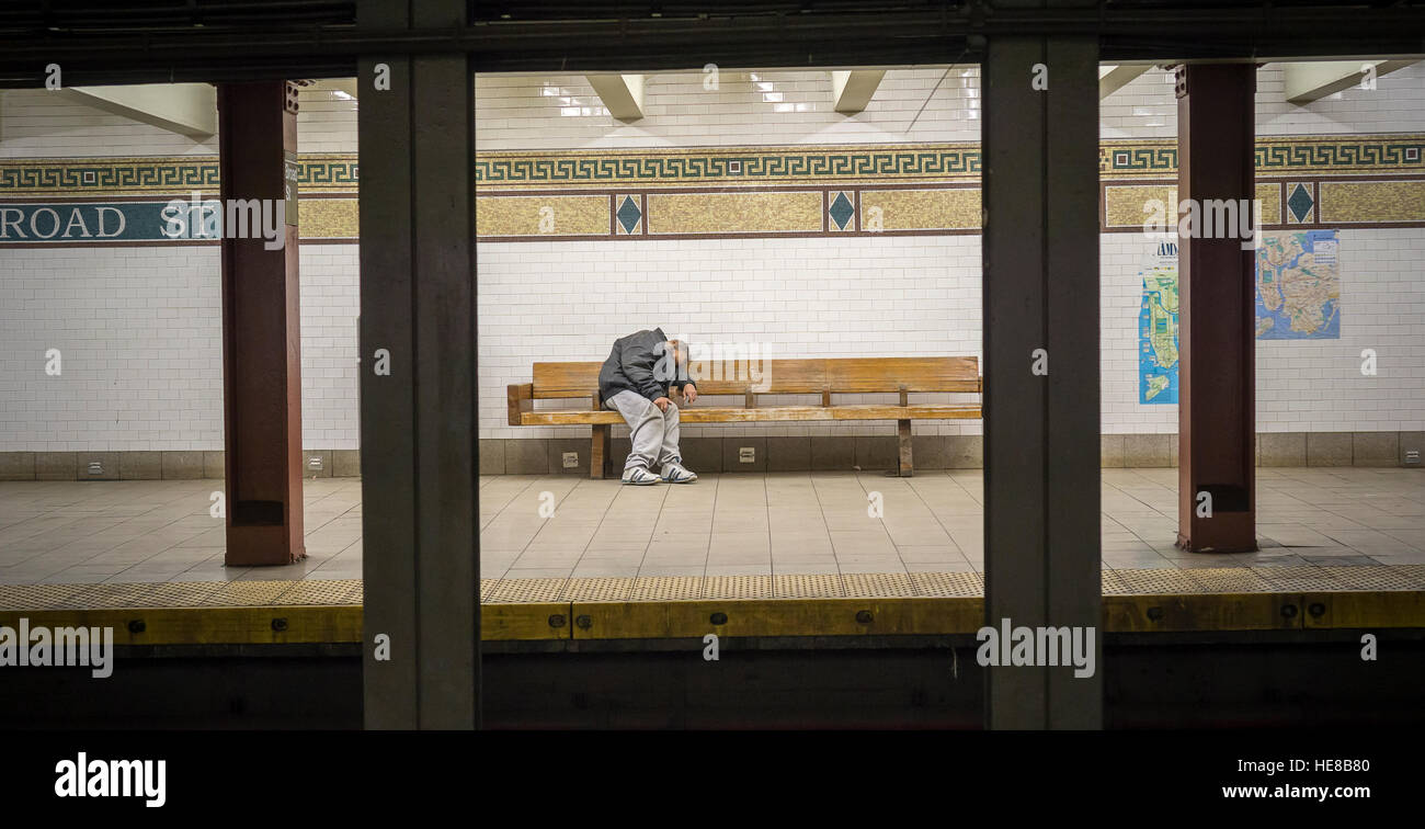 A homeless individual sleeps on a bench in a subway station in New York ...