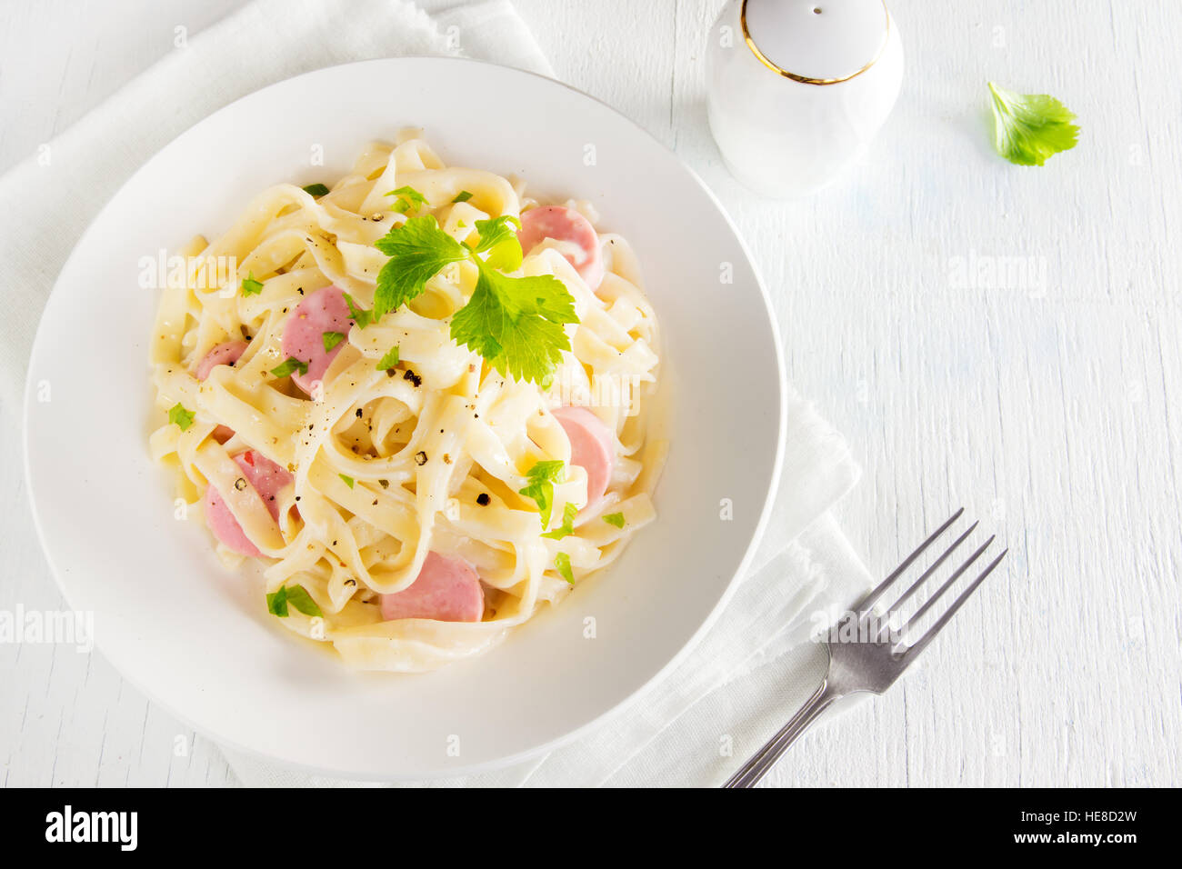 Alfredo tagliatelle pasta with sausages and greens on white plate