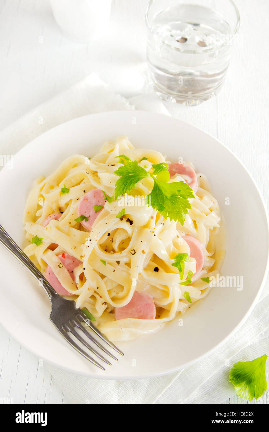 Alfredo tagliatelle pasta with sausages and greens on white plate