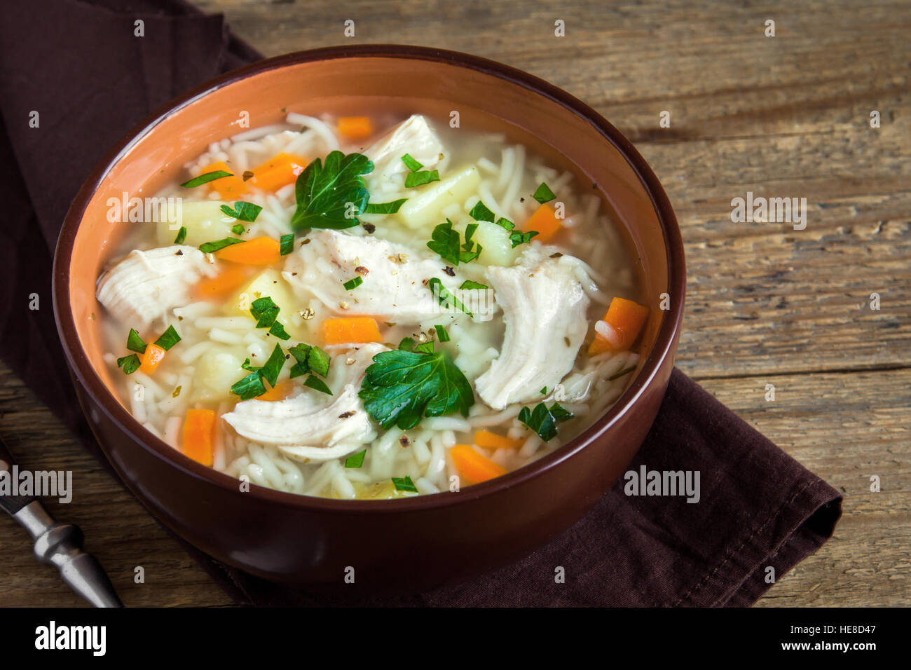 Chicken soup with noodles and vegetables in bowl over rustic wooden