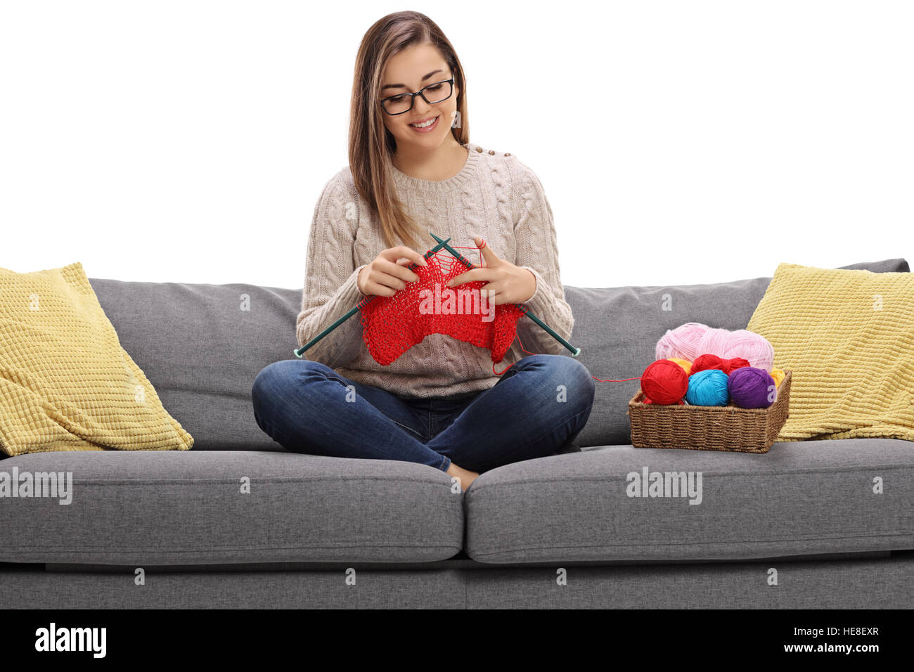 Happy young woman sitting on a sofa and knitting isolated on white ...