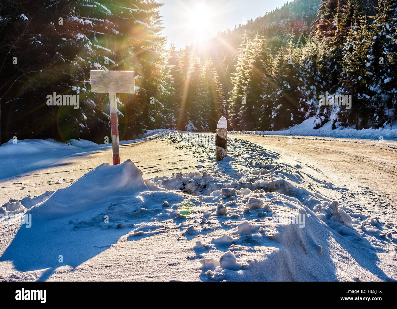 winter mountain landscape. wooden road sign on winding road that leads into the spruce forest covered with snow at sunrise Stock Photo