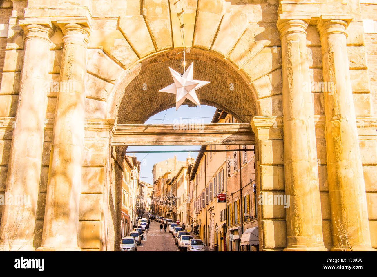 Christmas Star hangs from gate 'Porta Valbona' in the walled Medieval city of Urbino, Marche Region, Italy. Street 'via Mazzini' behind. Stock Photo