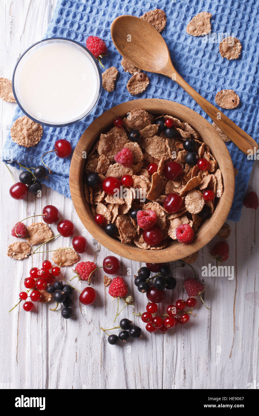 muesli with fresh berries in a wooden bowl and milk on the table. vertical top view Stock Photo