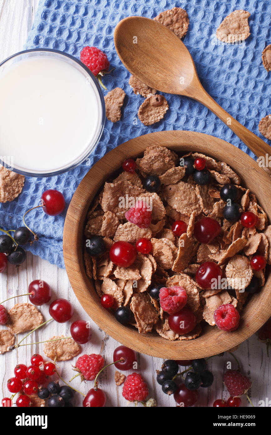 Granola with fresh berries in a wooden bowl and milk on the table. vertical top view Stock Photo