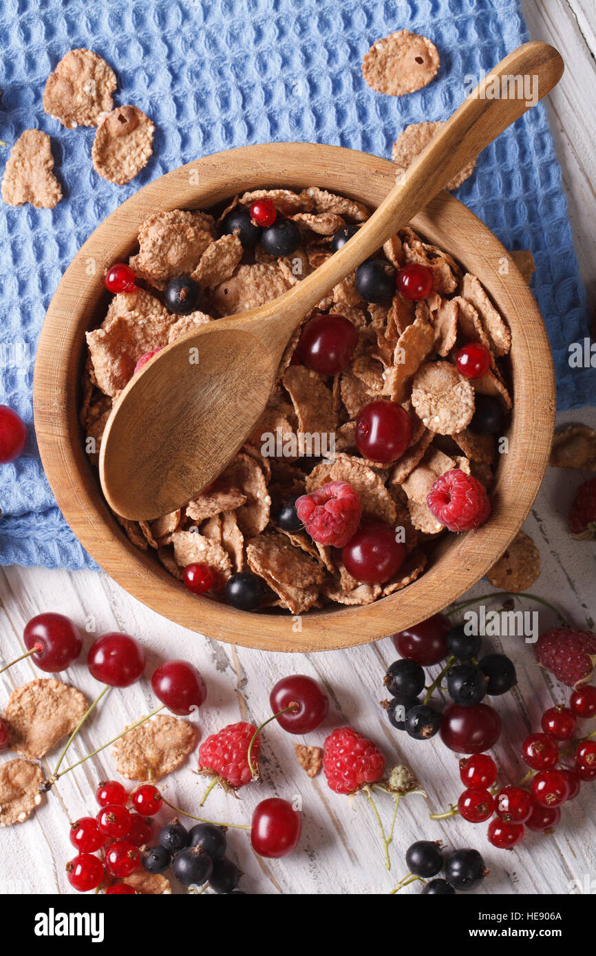 Muesli with fresh berries close up in a wooden bowl on the table. Vertical top view Stock Photo