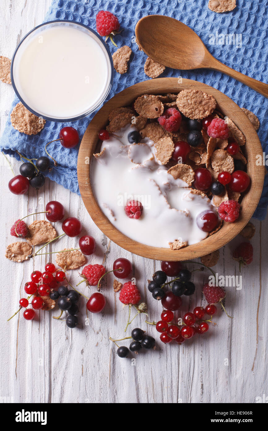 Granola with milk and fresh berries close up in a wooden bowl. vertical top view Stock Photo