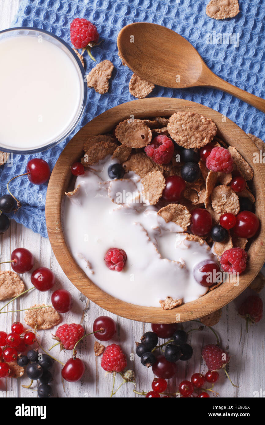Muesli with milk and fresh berries close up in a wooden bowl. vertical top view Stock Photo