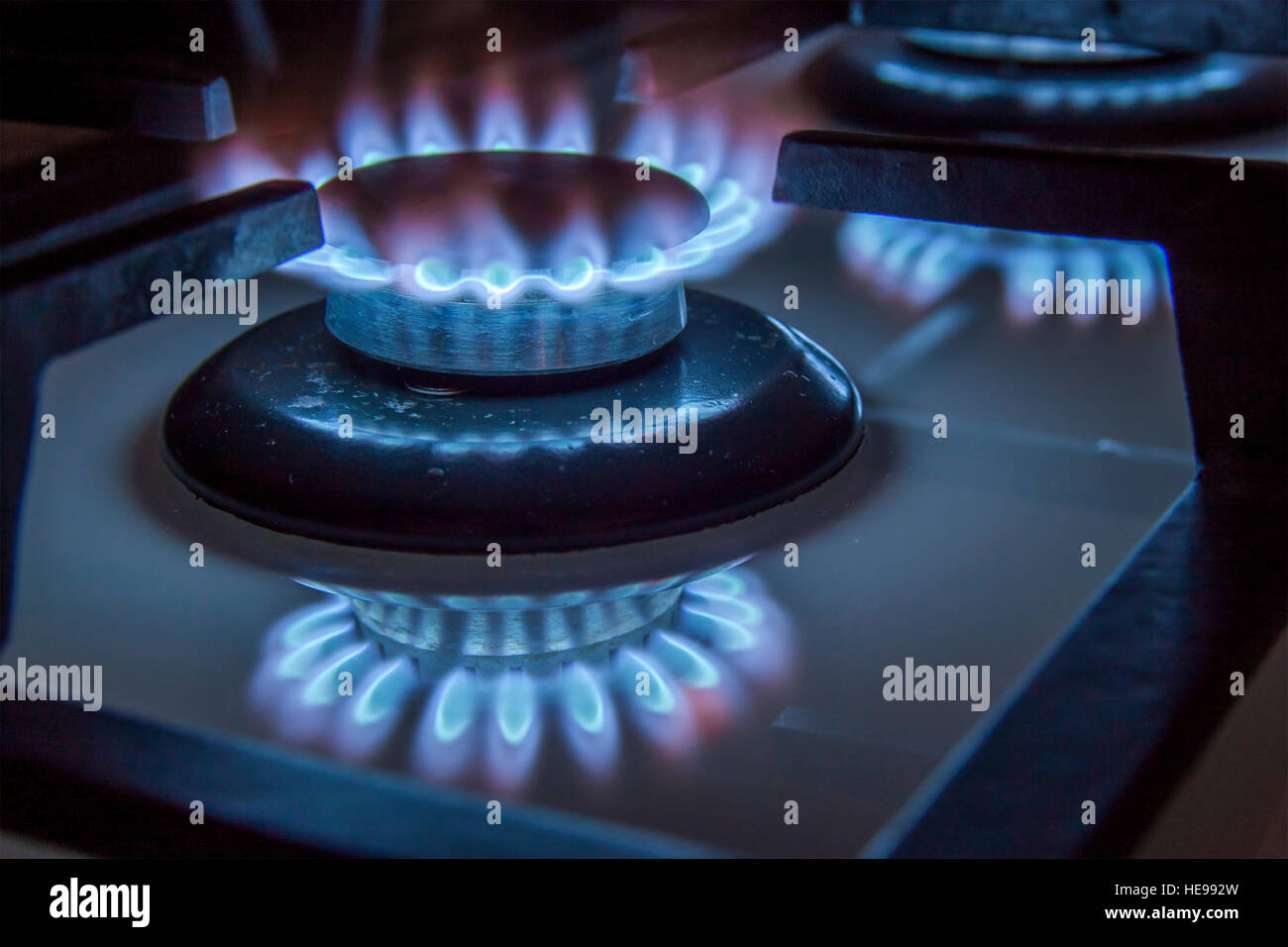 Burning gas stove hob blue flames close up in the dark on a black