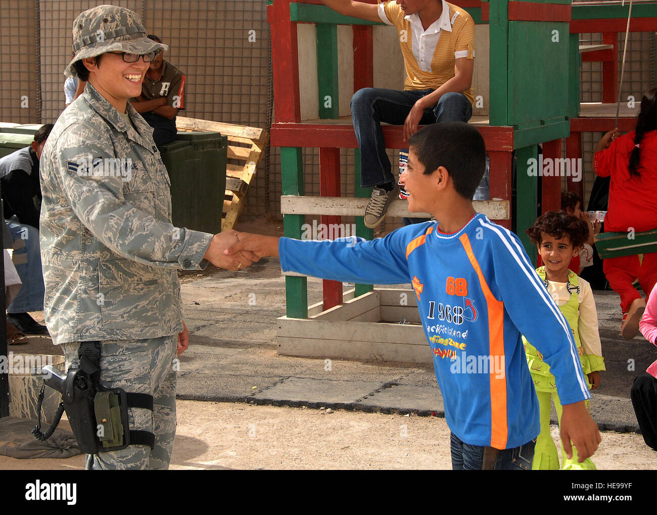 Camp Bucca, Iraq -- Airman 1st Class Martina Malone, a Security Forces member assigned to the 887th Expeditionary Security Forces Squadron, receives a handshake from an Iraqi boy waiting to visit his father at the Theater Internment Facility (TIF) at Camp Bucca, Iraq, on Sept. 29. The 887th ESFS controls access to prisoners at the TIF and processes visitation procedures for family members. The Air Force works side by side with Army Soldiers in manning the facility, which houses more than 18,000 inmates. Airman Malone is deployed from Dyess Air Force Base, Texas. Tech. Sgt. Raheem Moore) Stock Photo