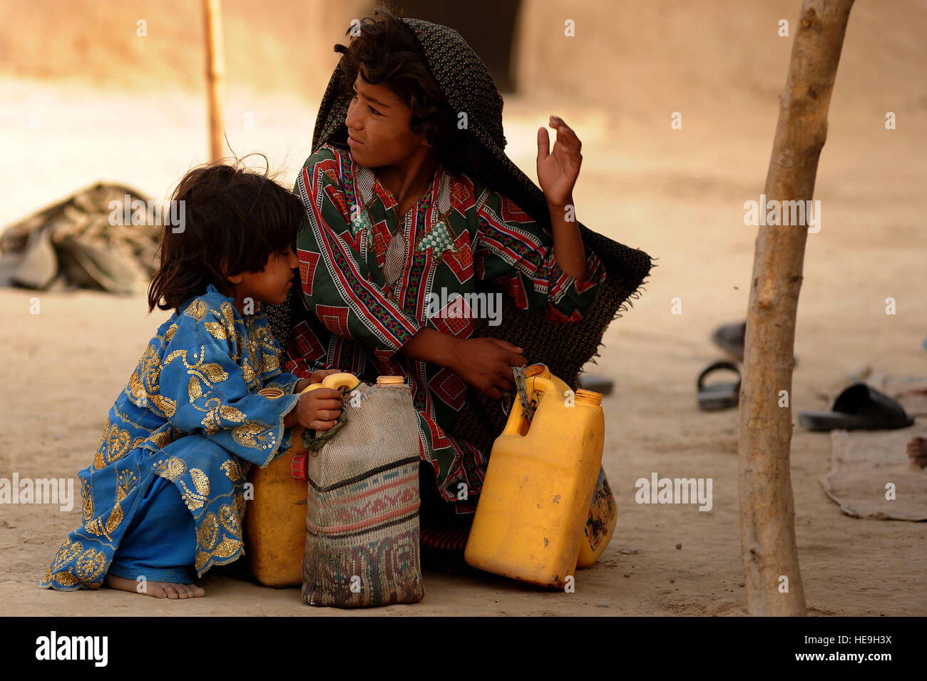 A young Afghan girl and her sister gather jugs of water to prepare chai tea for village elders, June 26, Dand District, Kandahar, Afghanistan. Stock Photo