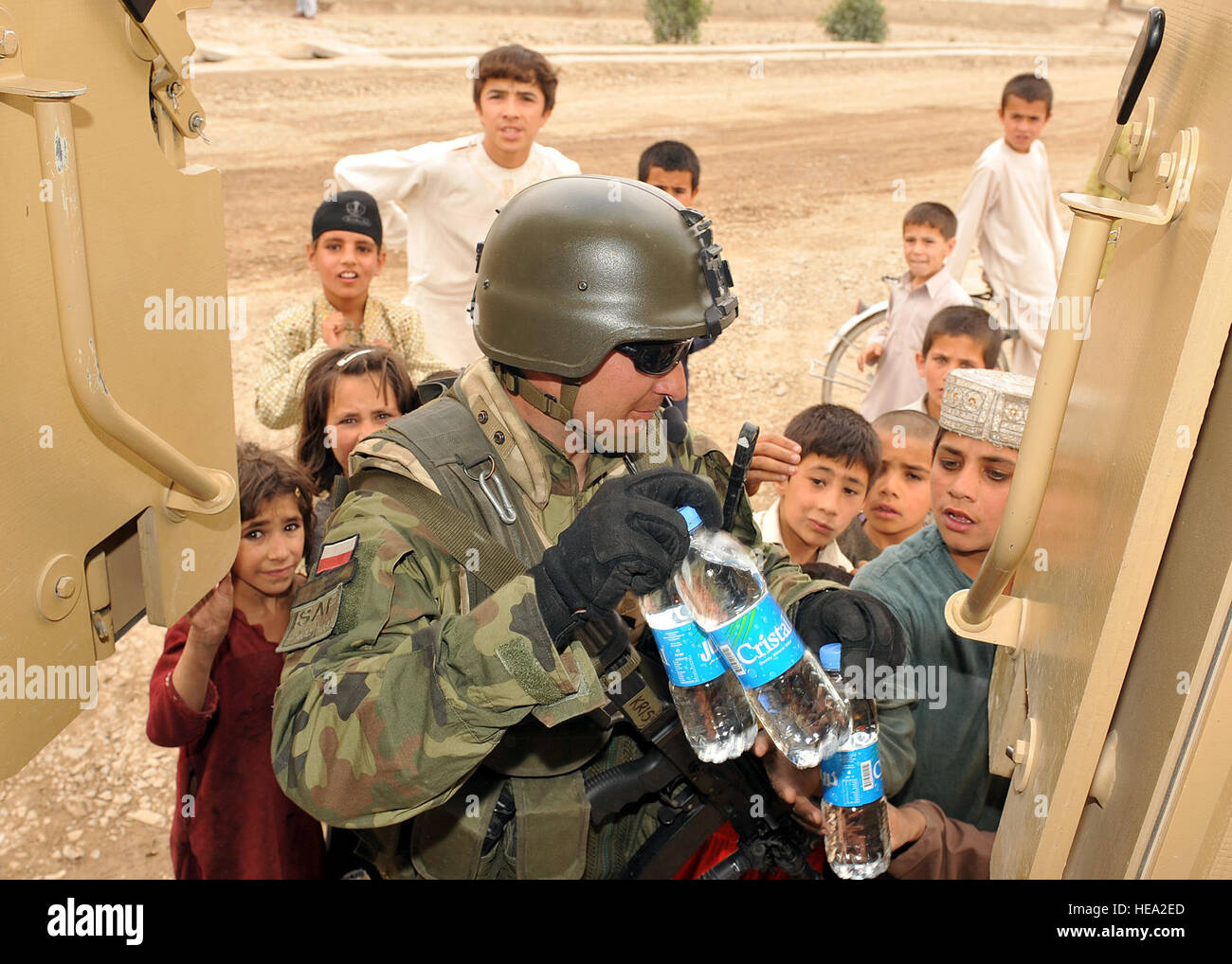 GHAZNI PROVINCE, Afghanistan– A Polish soldier distributes water to Afghan children during a visit to Returnee village located in Ghazni province, June 26. Return village houses displaced Afghan families, who previously fled their homes in search more secure and more stable areas to live in.  U.S. Air Force Tech Sgt. J.T. May III, Ghazni Provincial Reconstruction Team Public Affairs) Stock Photo